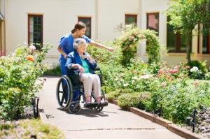 Aufnahme eines Bewohners und einer Krankenschwester im Garten des Altenheims. Sie benennen die Blumen, während sie gehen. 