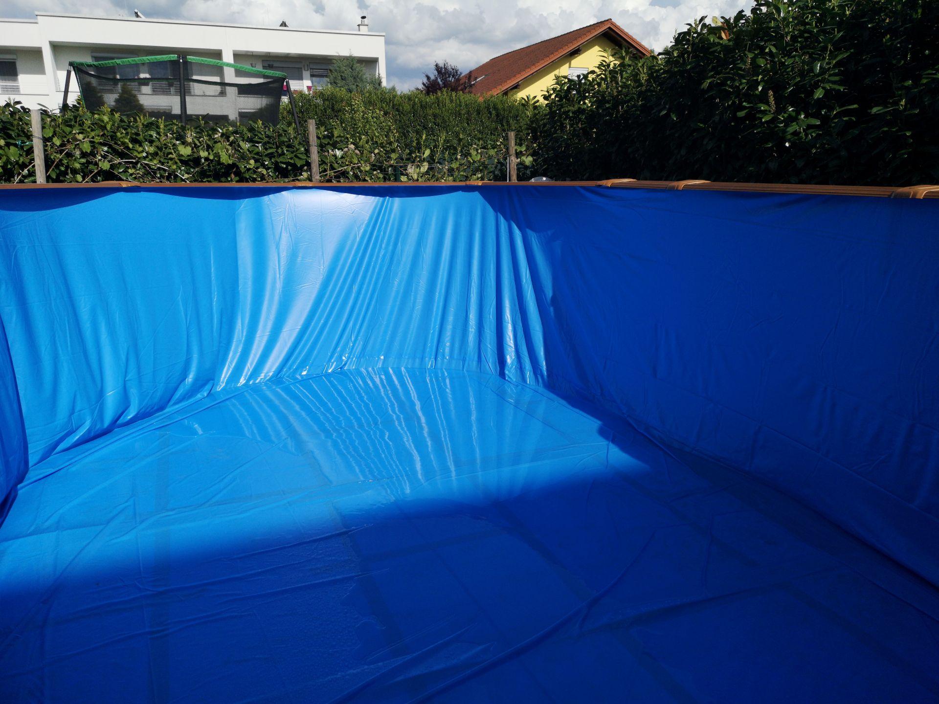 Blauer leerer Pool mit frisch ausgelegter Poolfolie vor dem Befuellen im Garten